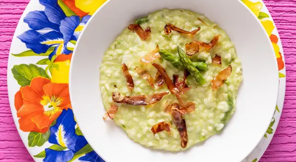 Un cremoso risotto asparagi e speck, guarnito con punte di asparagi freschi e croccanti sfoglie di speck.