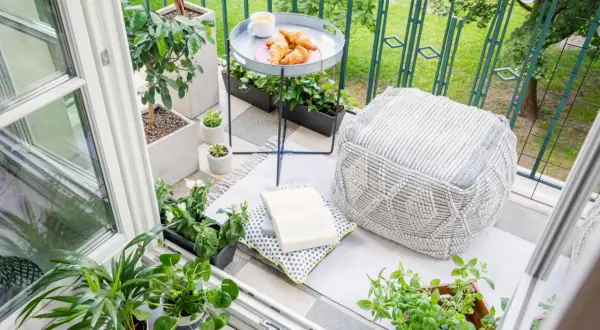 Gemütliche Balkon Ideen: Pflanzen, Kissen, Hocker und ein Tablett mit Croissants laden zum Verweilen ein.