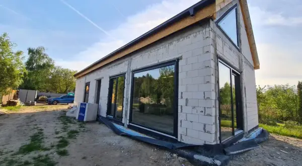 Nowy dom w stanie surowym zamkniętym, z dużymi oknami i dachem.