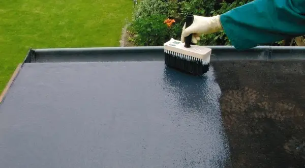 Mit einem Pinsel wird ein Bitumen-Voranstrich auf eine flache Dachfläche aufgetragen.