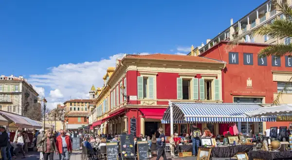En livlig marknad i en nice gamla stan med färgglada byggnader, uteserveringar och folk som strosar.