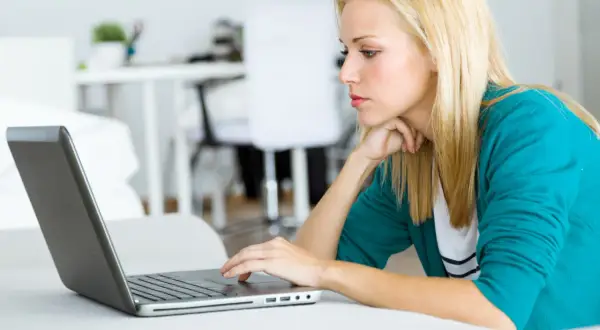 Kobieta z blond włosami pracuje na laptopie, analizując dokumenty dotyczące spłaconego komornika i kredytu hipotecznego.