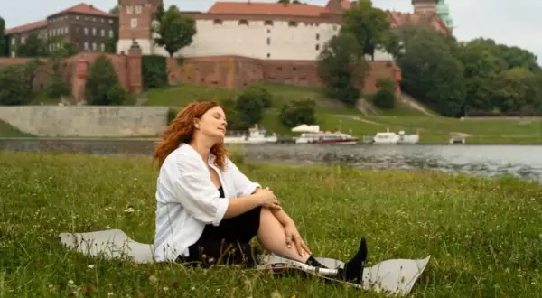 Kobieta z rudymi włosami odpoczywa na trawie z widokiem na Wawel. Idealne miejsce, by zastanowić się, gdzie na Wielkanoc.