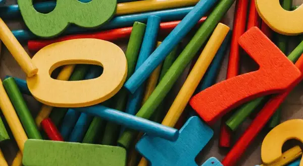 Bunte Holzfiguren und Stäbchen, die ein Helfersystem Grundschule bilden. Zahlen wie 0, 7 und 8 sind erkennbar.