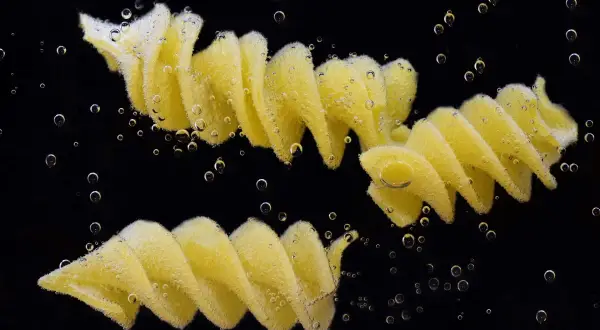 Dwa makarony fusilli gotujące się w wodzie, otoczone bąbelkami. Idealny przykład, jak ugotować makaron.