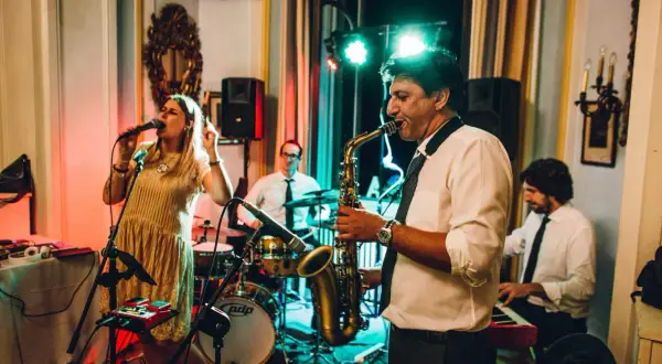 Una band suona musica dal vivo per un matrimonio. La cantante è in primo piano, mentre un sassofonista, un batterista e un tastierista completano il gruppo.