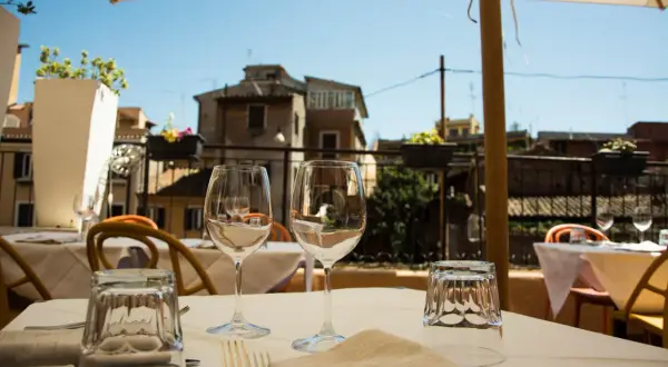 Tavola apparecchiata con bicchieri e posate in un ristorante all'aperto, con vista sui tetti di Roma. Un'atmosfera perfetta per scoprire i migliori ristoranti di Roma.