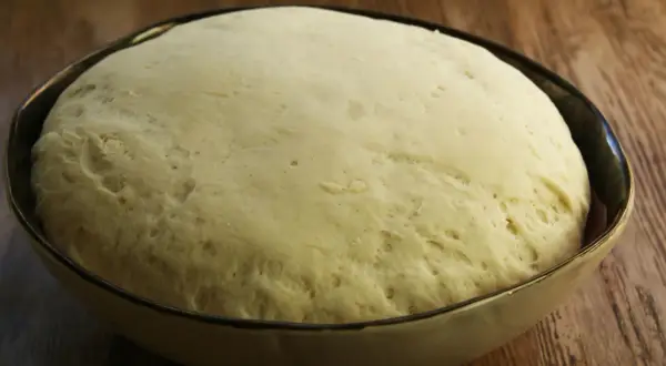Puszyste ciasto drożdżowe w misce, gotowe na idealne ciasto na pizzę. Widoczne pęcherzyki powietrza świadczą o jego lekkości.