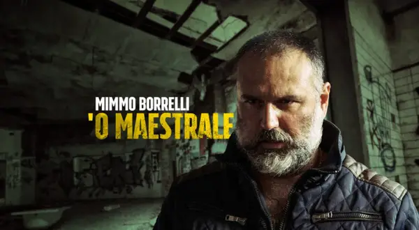 Mimmo Borrelli, 'O Maestrale, in un'ambientazione che ricorda Gomorra, con graffiti e un'atmosfera cupa.