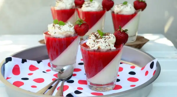Panna cotta z truskawkami i bitą śmietaną w szklankach, udekorowana miętą i czekoladą.