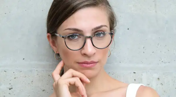 Kobieta w okularach o okrągłych, jasnych oprawkach, opierająca dłoń na policzku.