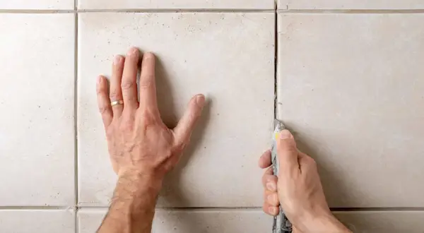 Main tenant utilise un cutter pour enlever des joints de carrelage en ciment.