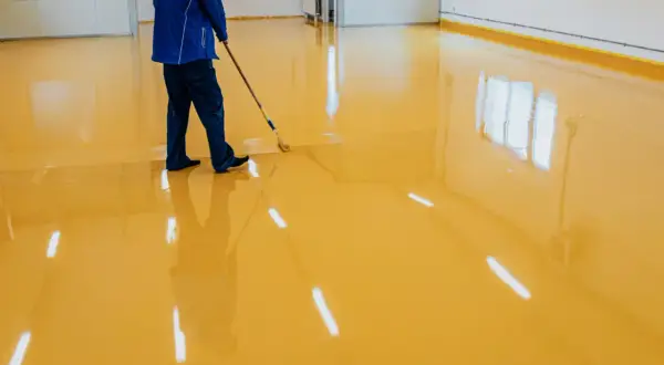 Operaio stende resina poliuretanica o epossidica gialla su un pavimento lucido, creando un ambiente moderno e resistente.