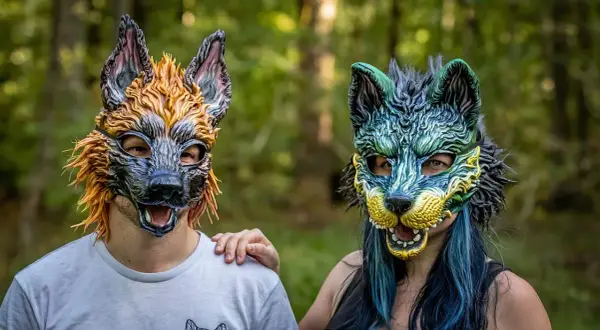 Dwie osoby w maskach wilków, symbolizujące tożsamość therian. Jedna w odcieniach pomarańczu, druga w zieleni i błękicie.