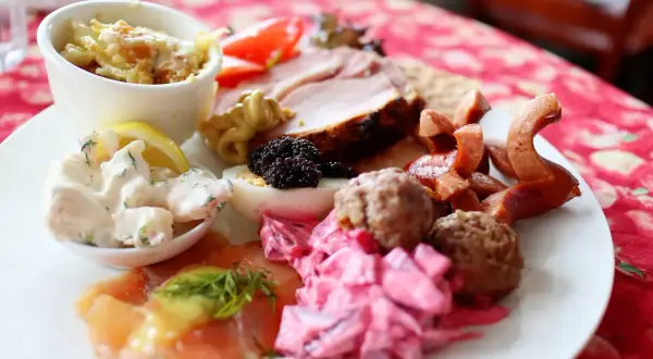 En härlig tallrik med godsaker på julbordet: lax, köttbullar, sill, ägg, rödbetor, korv och en liten skål med gratäng.