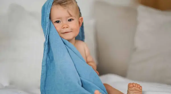 Ein süßes Baby von 12 Monaten, eingewickelt in ein blaues Tuch, schaut neugierig in die Kamera.