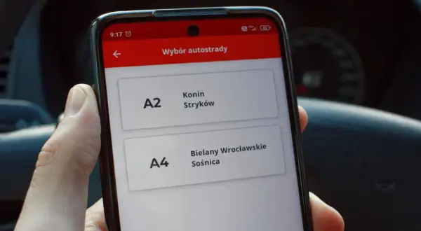 Dłoń trzyma smartfon z aplikacją do wyboru autostrady A2 Konin-Stryków i A4 Bielany Wrocławskie-Sośnica.