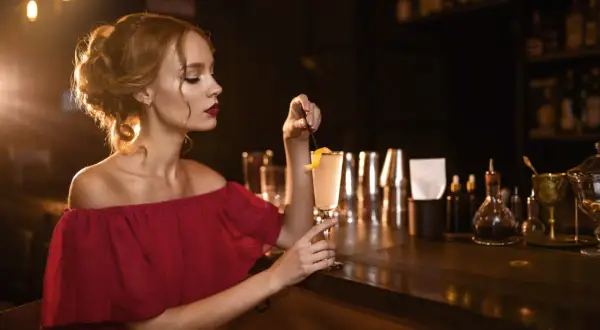 Elegancka kobieta w bordowej sukience z koktajlem w dłoni, idealne paznokcie do bordowej sukienki.