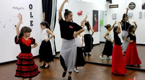 Niñas aprenden baile flamenco en una clase. La maestra las guía con movimientos elegantes.