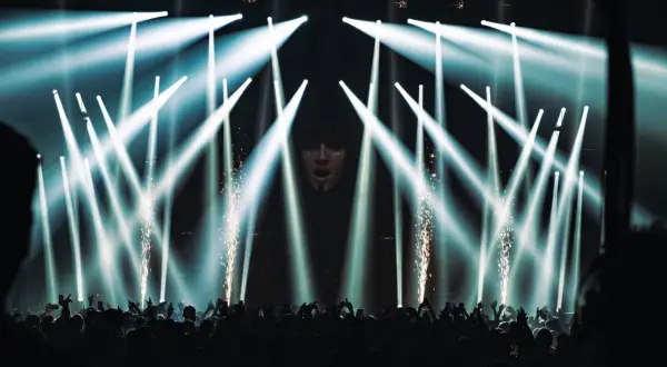 Koncert Apashe w Warszawie: tłum szaleje pod laserami i fajerwerkami, artysta na ekranie.