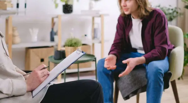 En person sitter och skriver på en clipboard medan en annan person pratar. En scen som kan symbolisera tvångstankar behandling.