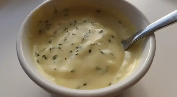 En skål med krämig, gul vegansk bearnaisesås med finhackade örter. Perfekt för ditt veganska bearnaisesås recept.