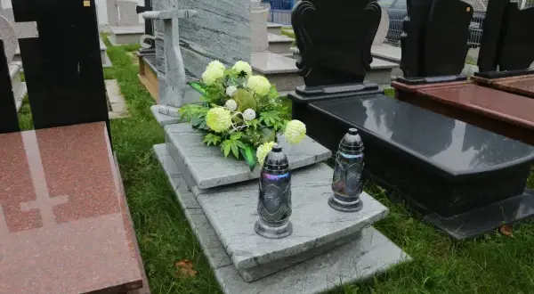 Elegancka dekoracja grobu bez pomnika: szare płyty, bukiet jasnych kwiatów i dwie znicze.