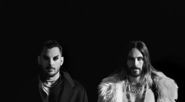 Jared Leto i Shannon Leto z 30 Seconds to Mars na czarno-białym zdjęciu. Jared w futrzanym płaszczu, Shannon w eleganckim płaszczu.