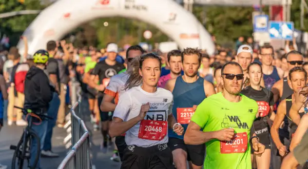 Uczestnicy biegu, realizujący swój plan treningowy maraton, mijają bramę startową.