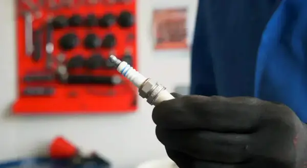 Main tenue une bougie d'allumage neuve, prête à être installée. Savoir quand changer les bougies d'allumage est essentiel pour le bon fonctionnement de votre moteur.