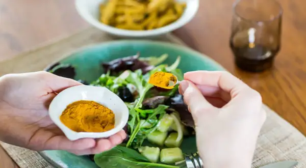 Mani aggiungono curcuma a un'insalata, sfruttando i curcuma e pepe nero benefici per un pasto sano.
