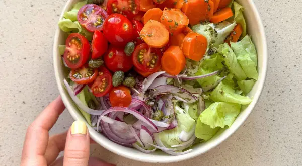 Deliciosa ensalada mediterránea con lechuga, tomates cherry, zanahoria, cebolla morada y alcaparras.