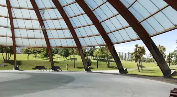 Estructura de madera y cristal en el parque de Eiris, con vistas a césped, árboles y edificios.