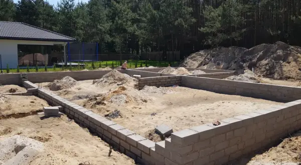 Fundamenty domu w budowie. Piasek, bloczki betonowe i kopce ziemi. To pierwszy krok, od czego zacząć budowę domu.