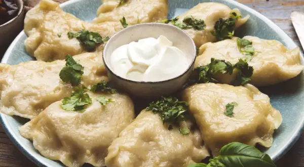 Pyszne pierogi ze szpinakiem i serem feta, udekorowane natką pietruszki, podane z kleksem śmietany.