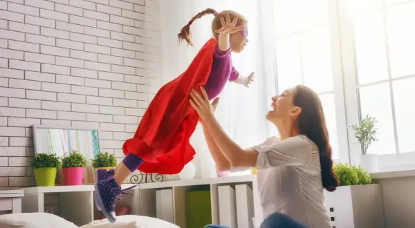 Mama rzuca córkę w stroju superbohaterki w powietrze. Radość i zabawa w pokoju.