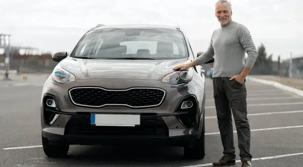 Starszy mężczyzna stoi obok brązowego SUV-a na parkingu.