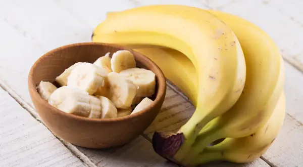 Kawałek banana w drewnianej miseczce obok całych bananów. Poznaj banan wartości odżywcze i ciesz się zdrową przekąską.