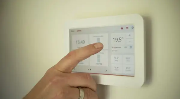 Palec dotyka ekranu termostatu, sprawdzając, ile prądu zużywa 4 osobowa rodzina miesięcznie.