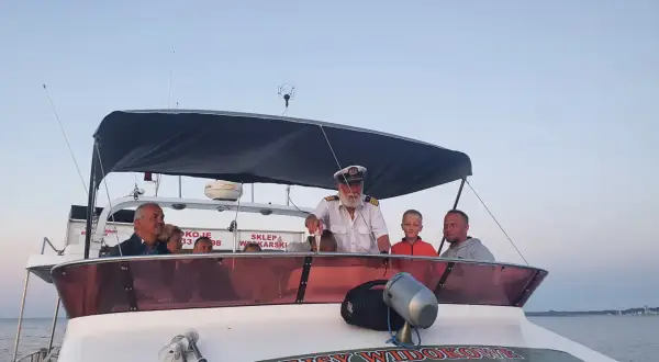 Kapitan z lornetką na pokładzie łodzi zaprasza na rejsy statkiem we Władysławowie. Rodzina cieszy się widokiem.