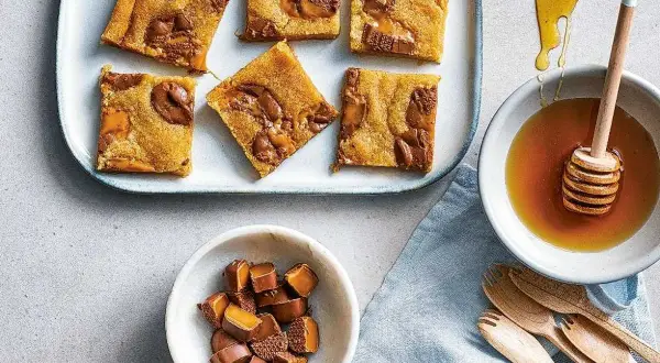 Enkla dumlekakor med chokladbitar på en bricka, bredvid en skål med honung och en skål med hackade dumlekolor.