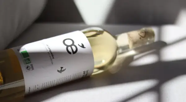 Flasche mit hellem Wein, Etikett mit "8" und Vögeln, Bio-Siegel. Ein Wein ohne Sulfite, der die Natur ehrt.