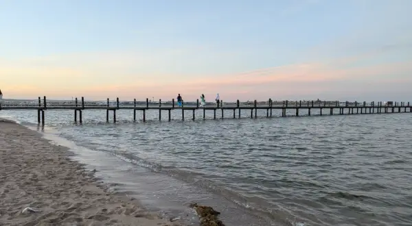 Piękna egipska pogoda we wrześniu. Długie molo na spokojnym morzu, piasek na plaży i pastelowe niebo.