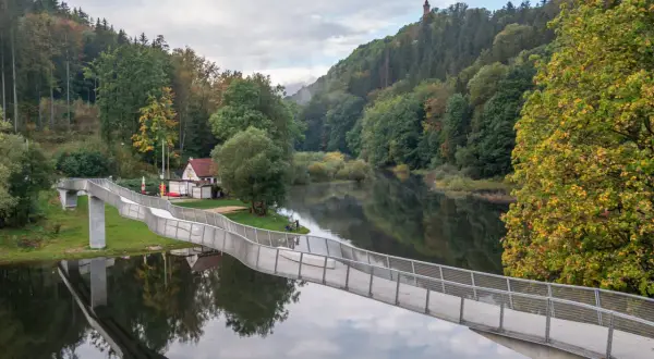 Nowoczesny most nad rzeką, otoczony jesiennym lasem. W oddali wieża widokowa, jedna z atrakcji Wałbrzycha i okolic.