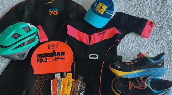 Triathlon gear laid out: wetsuit, helmet, swim cap, tri suit, running shoes, and energy gels. Everything you need to know what to wear for a triathlon.