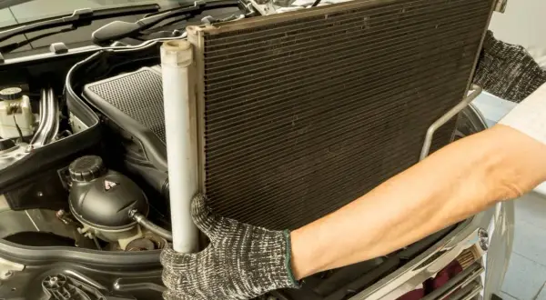 Mechanik wyjmuje chłodnicę klimatyzacji. Sprawdź wymiana chłodnicy klimatyzacji cena.