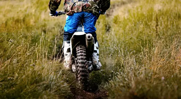 Motocyklista w stroju off-roadowym jedzie po trawiastym torze.
