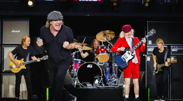 Zespół AC/DC na scenie, grający swoje kultowe utwory. Wokalista w czapce, gitarzysta w czerwonym stroju.