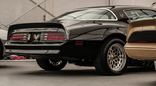 Błyszczący czarny muscle car z charakterystycznym spojlerem i felgami. Obok złoty klasyk.