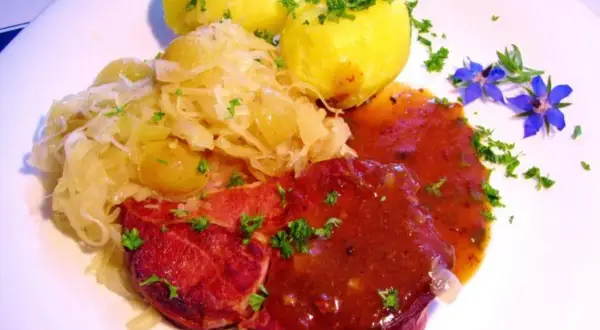 Gekochte Rippchen zubereiten: Herzhaftes Gericht mit deftigen Rippchen, Sauerkraut und Kartoffeln, garniert mit Petersilie und blauen Blüten.
